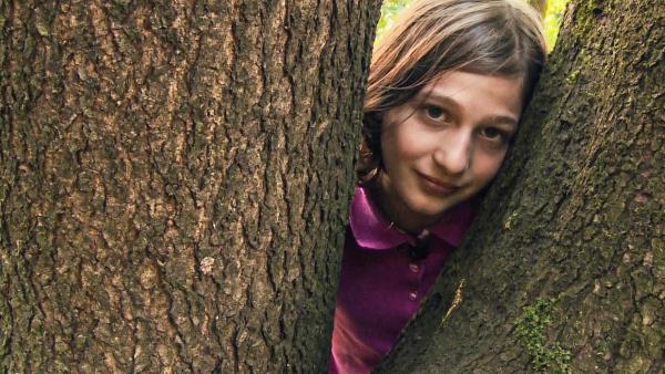 Yael schaut zwischen zwei riesigen Baumstämmen in die Kamera. | Rechte: ZDF