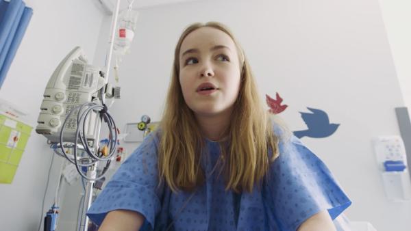 Jenny sitzt in ihrem Krankenhauszimmer auf dem Bett und erzählt. | Rechte: KiKA/9347-4732 Québec Inc