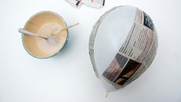 eine Schüssel  mit angerührtem Tapetnkleister, daneben ein Luftballon mit einigen aufgeklebten Zeitungsstreifen