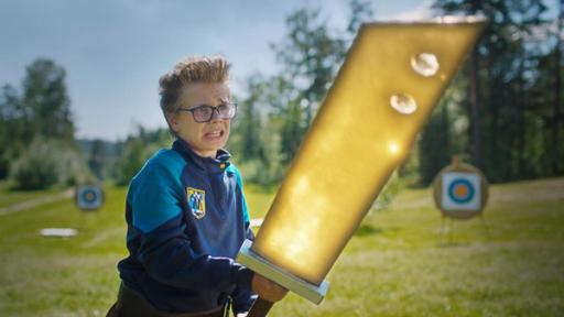 Uno steht mit ängstlichem Blick auf einer Wiese, die von Bäumen und Sträuchern umringt ist. Er hält angestrengt ein riesiges golden leuchtendes Schwert mit beiden Händen fest. Im Hintergrund stehen Zielscheiben.