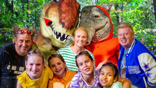 Tom Lehel, ein T-Rex, TanzTapir, Singa, Kindermusiker Volker Rosin und die TanzAlarm-Kids stehen mitten im Wald unfd lächeln in die Kamera.