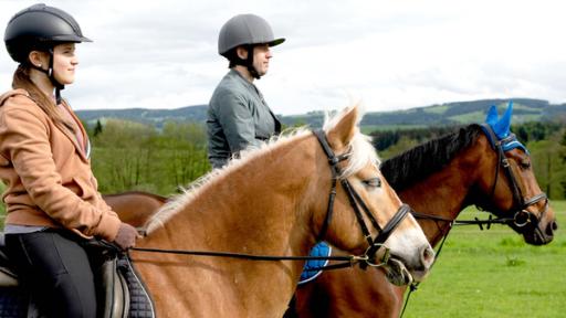 Zwei Reiter, ein junges Mädchen und ein Mann, sitzen auf ihren Pferden und schauen in die Landschaft.