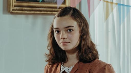 Clarissa trifft auf Anne Frank (Katharina Kron). Clarissa lächelt und hat einen alten Fussball in der Hand. Anne Frank schaut neutral und hält ein Buch in ihren Händen.