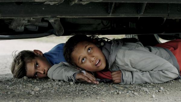 Nora (Naomi Hasselberg Thorsrud) und Simon (Oskar Lindquist) verstecken sich unter Tom und Julias Geländewagen. | Rechte: NDR/NordicStories