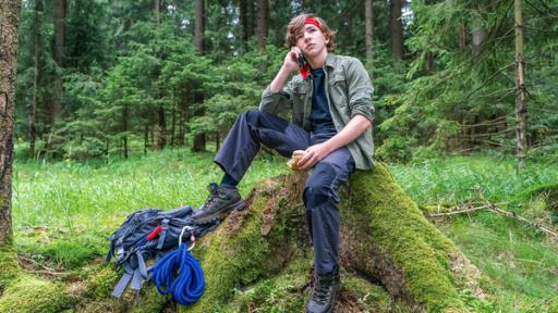 Mitten im Wald sitzt auf einem Baustumpf der siebzehnjährige Rob. Er trägt ein rotes Stirnband, typische Outdoor-Kleidung, zu seinen Füßen liegt ein Rucksack samt Seil und Kletterhaken. Mit selbstgewisser Mine telefoniert er über sein Handy, hält in seiner anderen Hand ein angebissenes Brötchen und scheint den Moment völlig entspannt zu genießen.