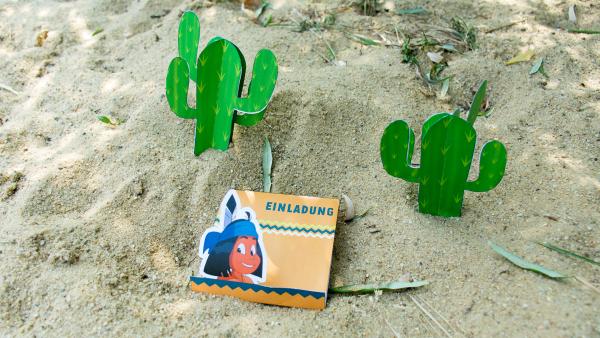 Eine Yakari - Geburtstagseinladungskarte steht mit Kakteen im Sand. | Rechte: KiKA